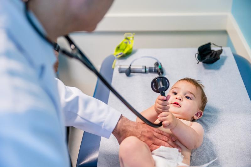 a cute baby holding onto a stethoscope with a doctor leaning over him